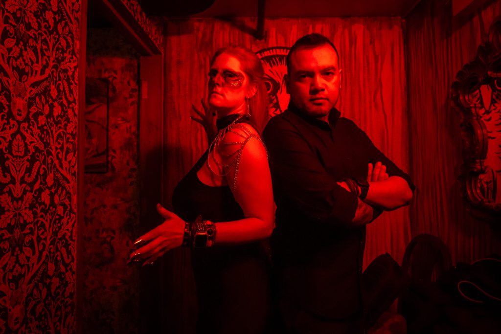 Emilie Bienne and AL Javier of BLOODFATE posing back to back in red light