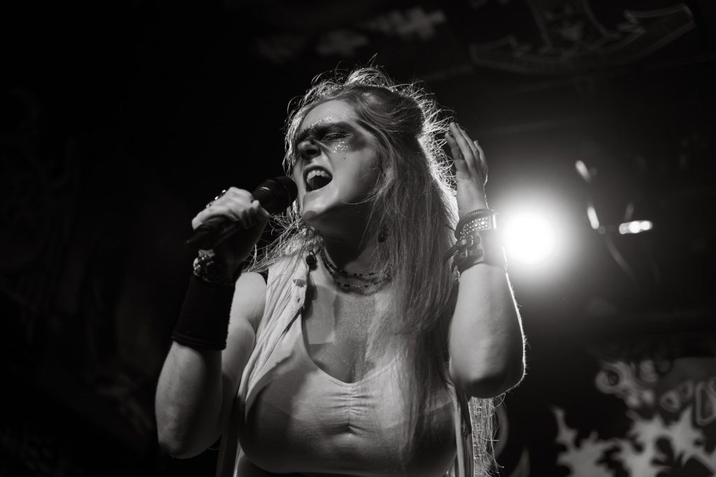 Black and white photo of Emilie Bienne of BLOODFATE singing live on stage